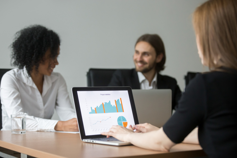 Três pessoas em uma sala de escritório com comutadores em uma reunião, analisando gráficos com métricas de Marketing de conteúdo.
